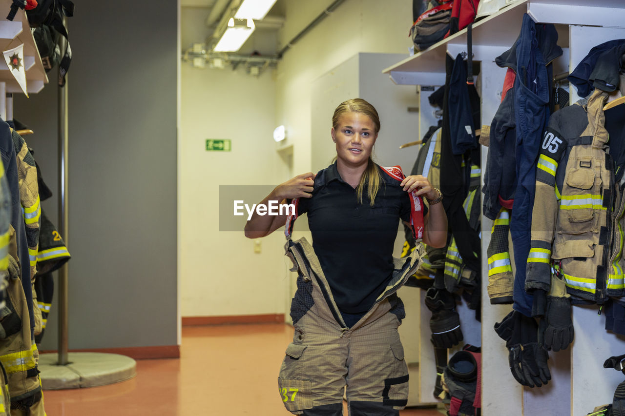Female firefighter putting protective workwear on in locker room