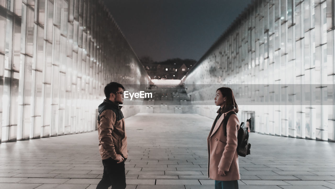 Couple standing on footpath in city at night