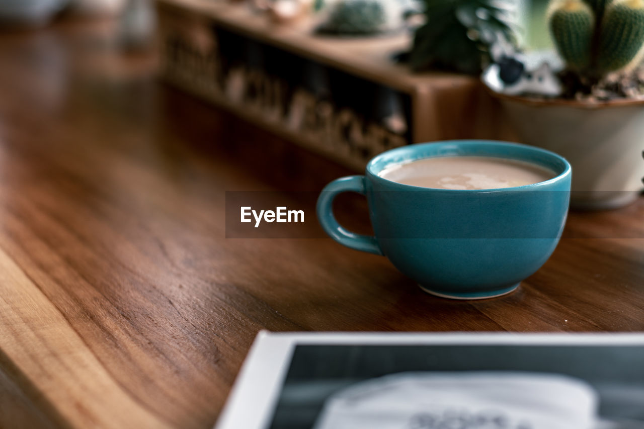 Close-up of coffee cup with potted plant on wooden table