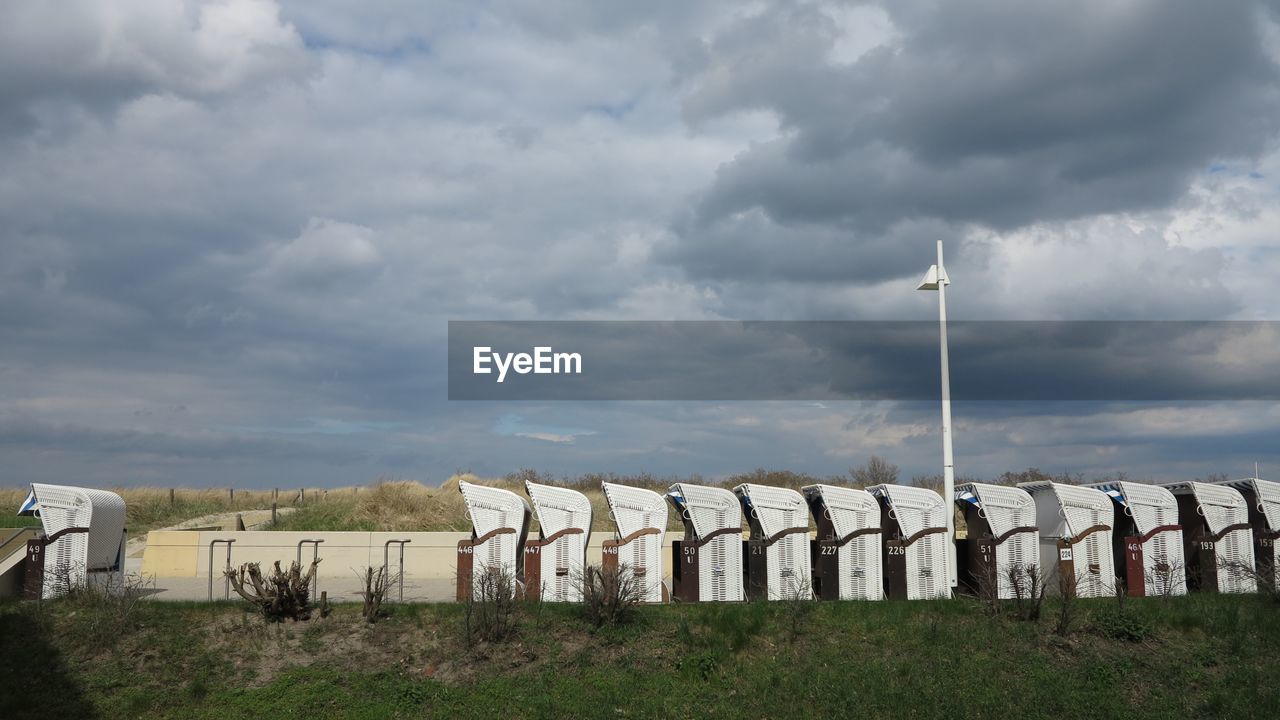 Hooded beach chairs on grassy field against cloudy sky