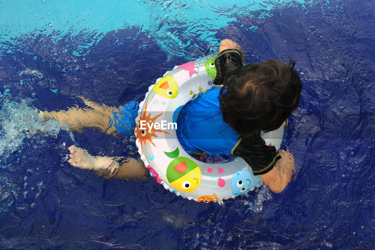 Rear view of boy floating with inflatable ring in swimming pool