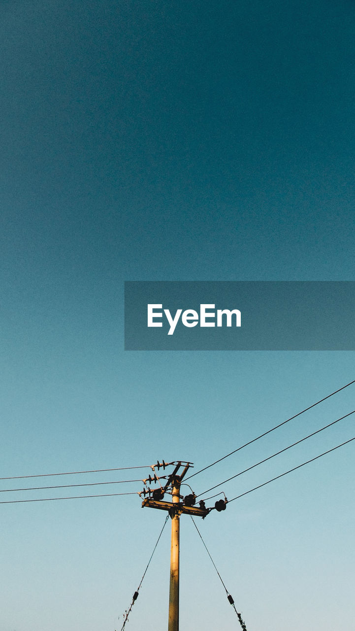 Low angle view of electricity pylon against clear blue sky