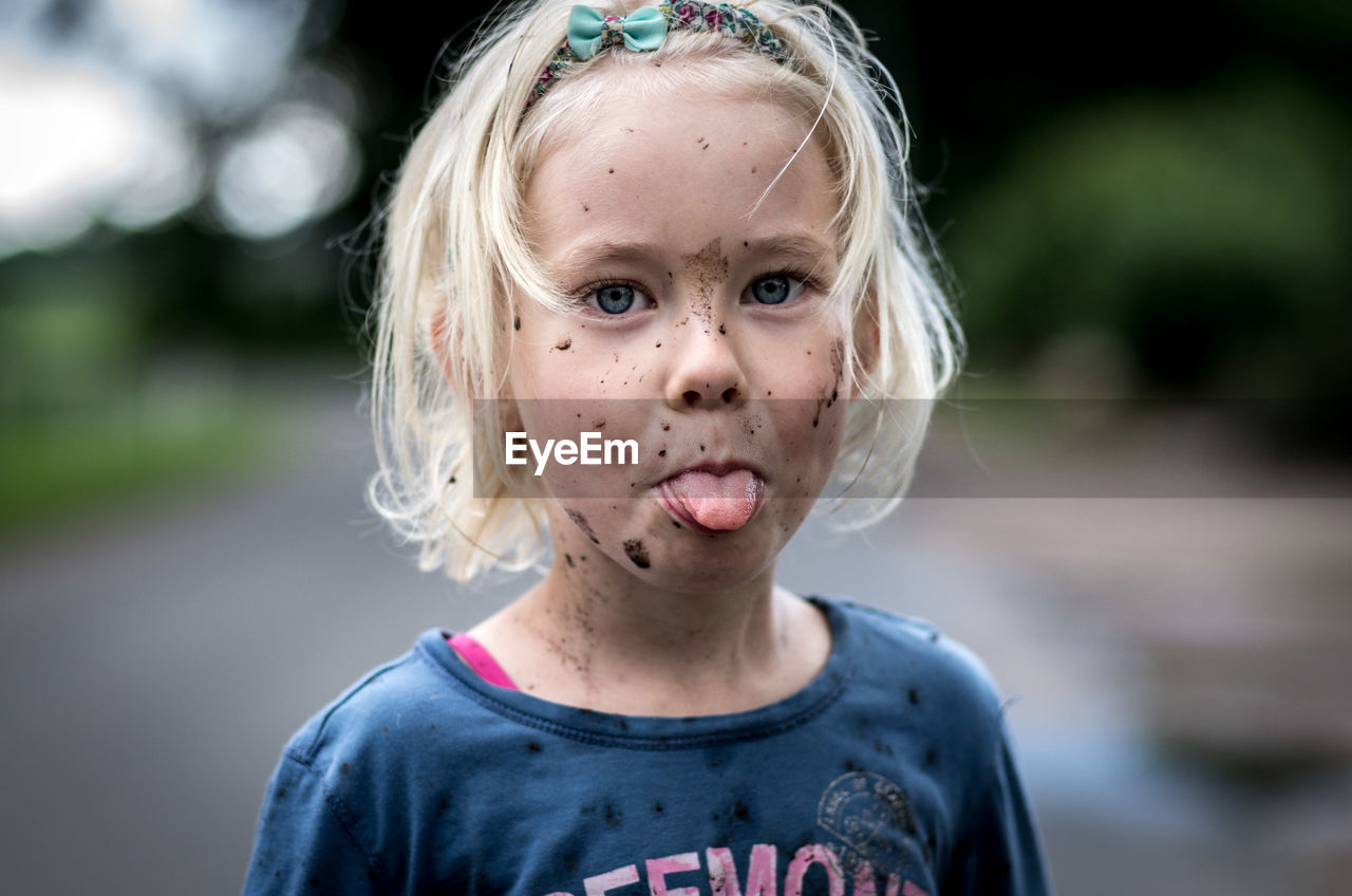 Portrait of cute girl with messy face sticking out tongue