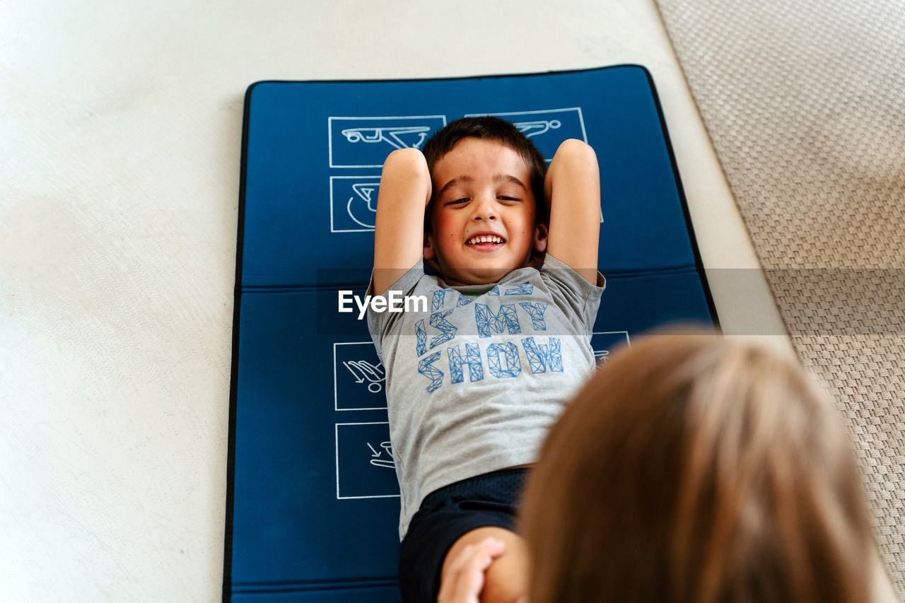 High angle positive little boy in sportswear with hands behind head doing sit ups on yoga mat