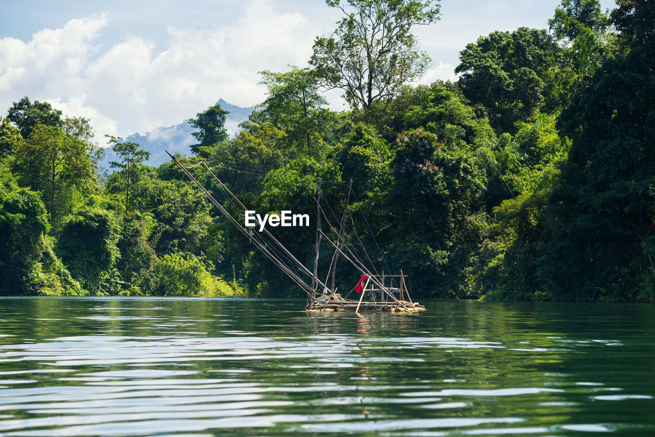 Fisherman tool on raft at lake by trees against sky