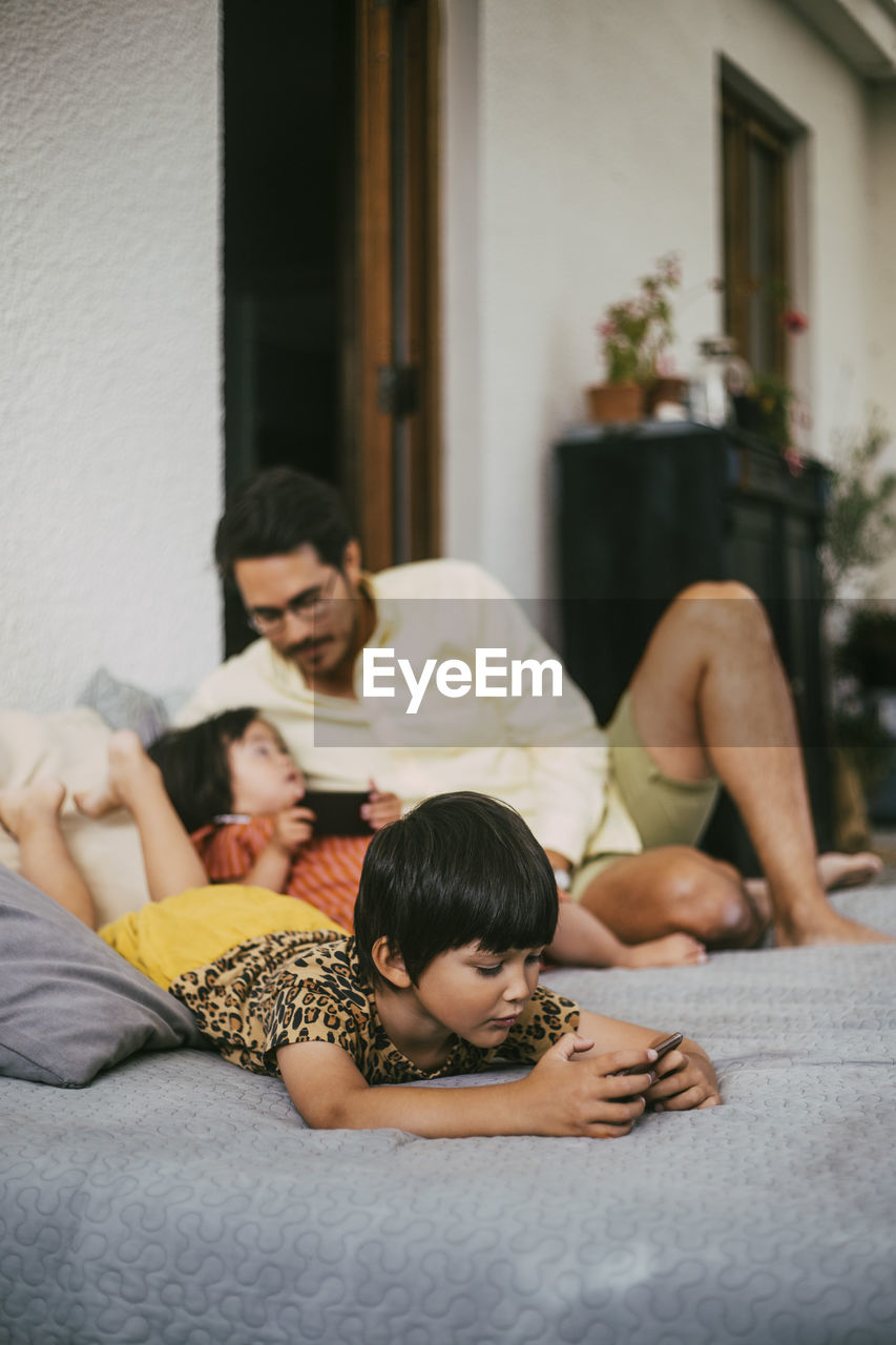 Girl using smart phone while down syndrome girl talking to father on sofa at home