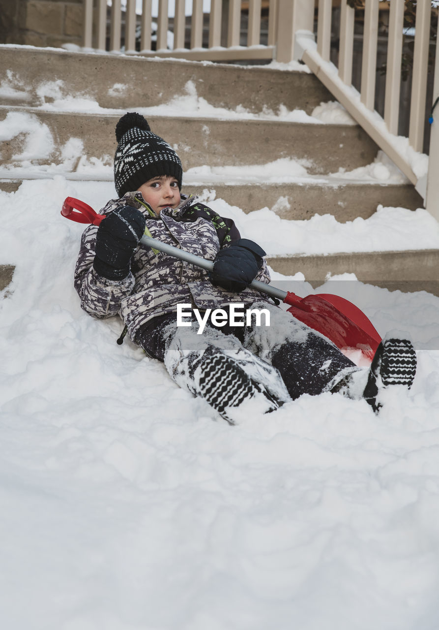 Portrait of boy with shovel lying on snowy steps
