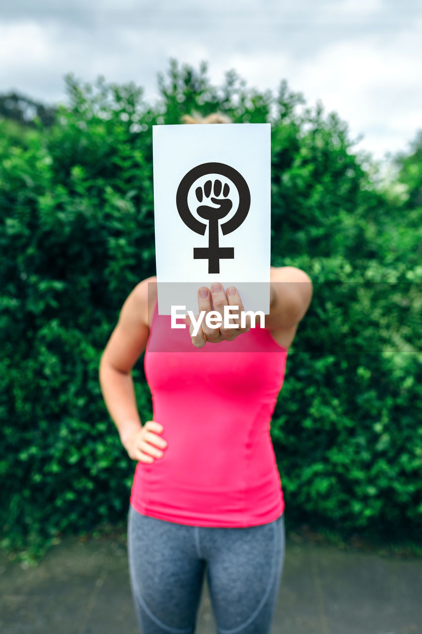 Women covering face with placard while standing against plant