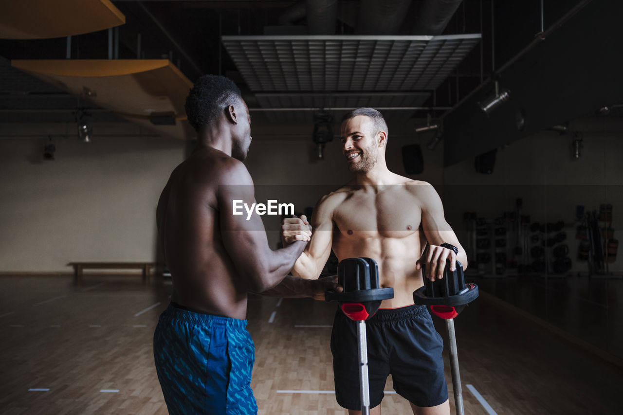 Smiling young sports people with barbell shaking hands in gym