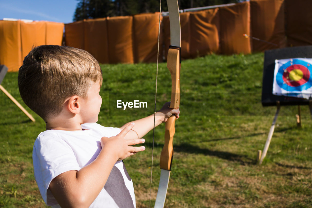 Boy using bow and arrow and shooting at the target outdoors.