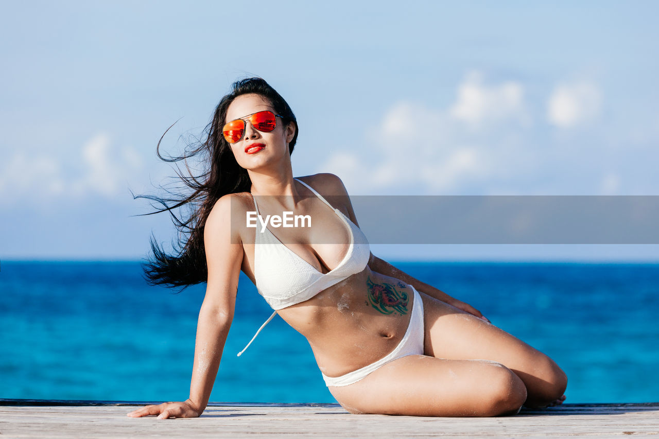 Portrait of smiling young woman standing at beach against sky