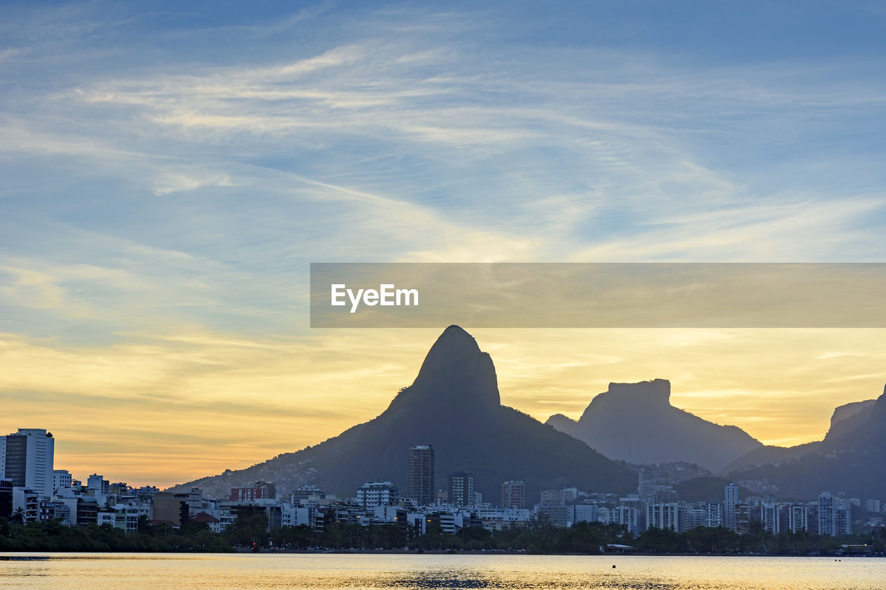 Scenic view of lake by buildings against sky during sunset