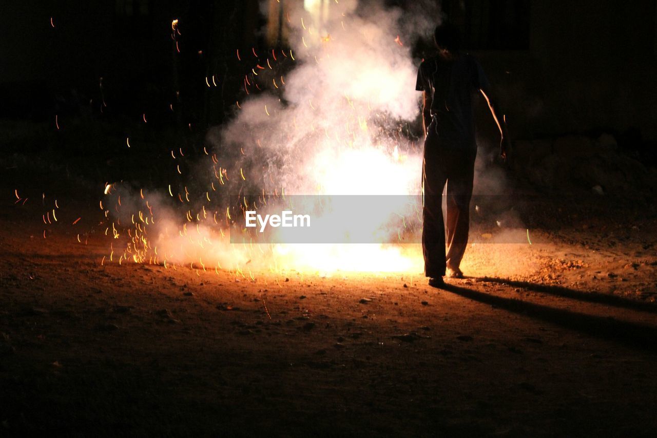 Rear view of man burning crackers on field at night