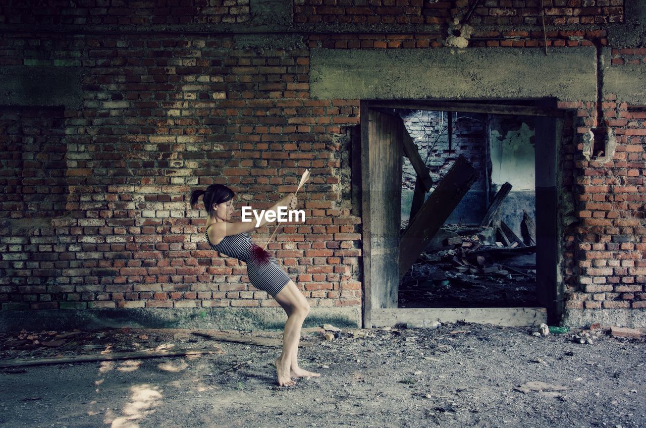 Digital compromise image of young woman killing herself with arrow by abandoned building
