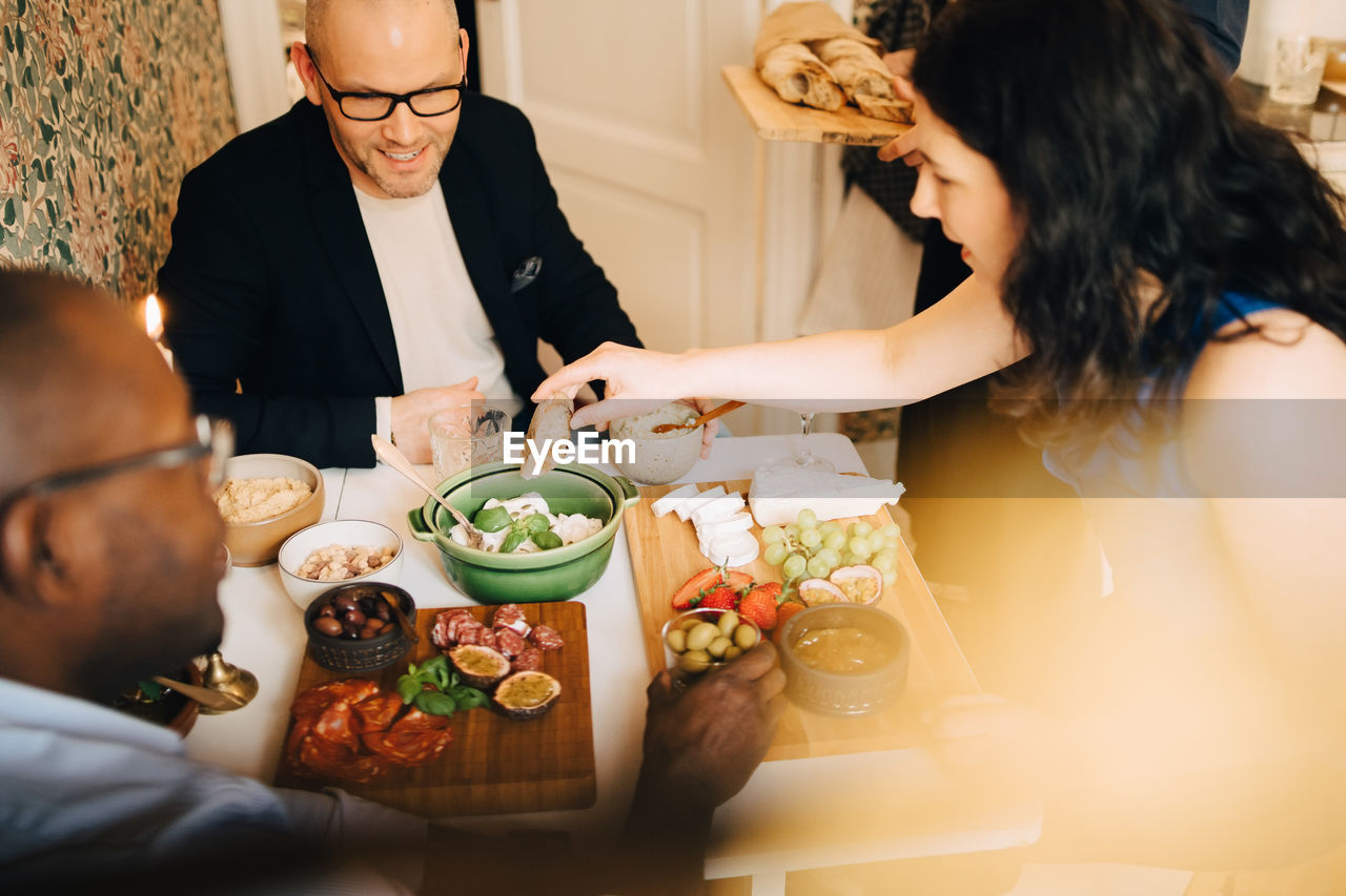 Woman sitting with male friends while having dinner during party at home