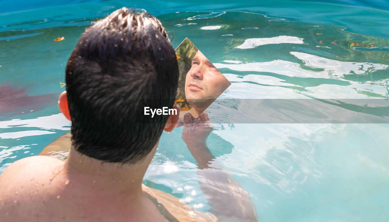 Reflection of man in mirror while sitting in swimming pool