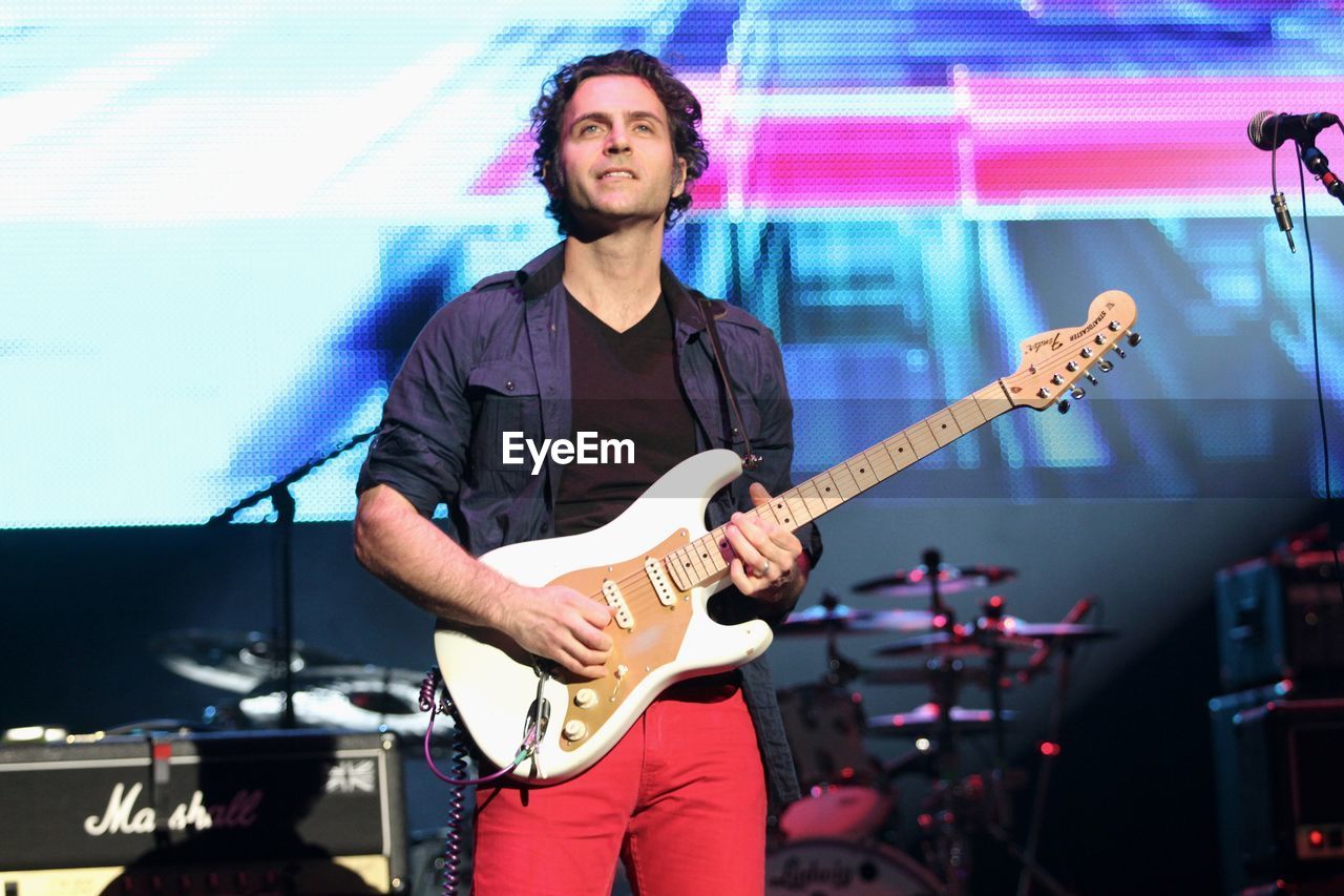 YOUNG MAN PLAYING GUITAR AT MUSIC CONCERT