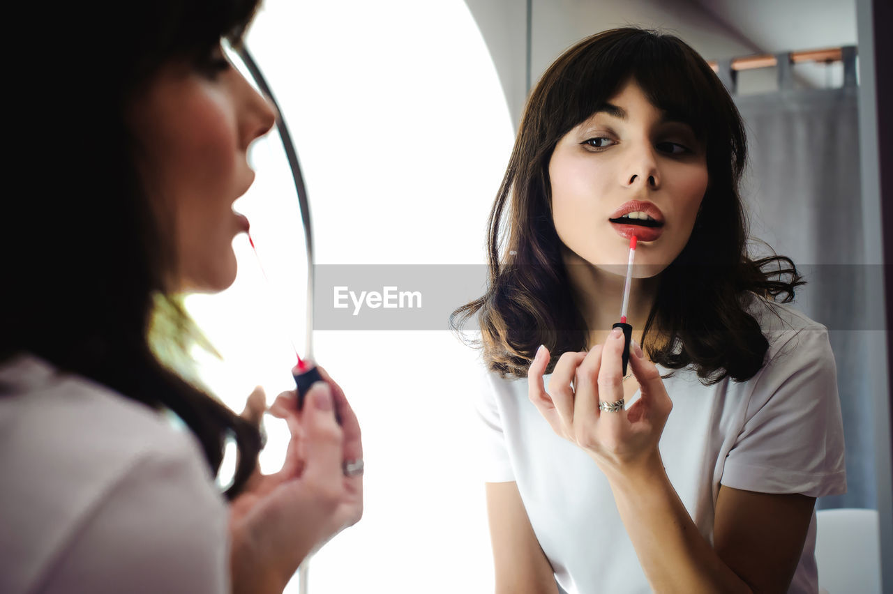 Close-up of young woman applying red lipstick in front of mirror at home