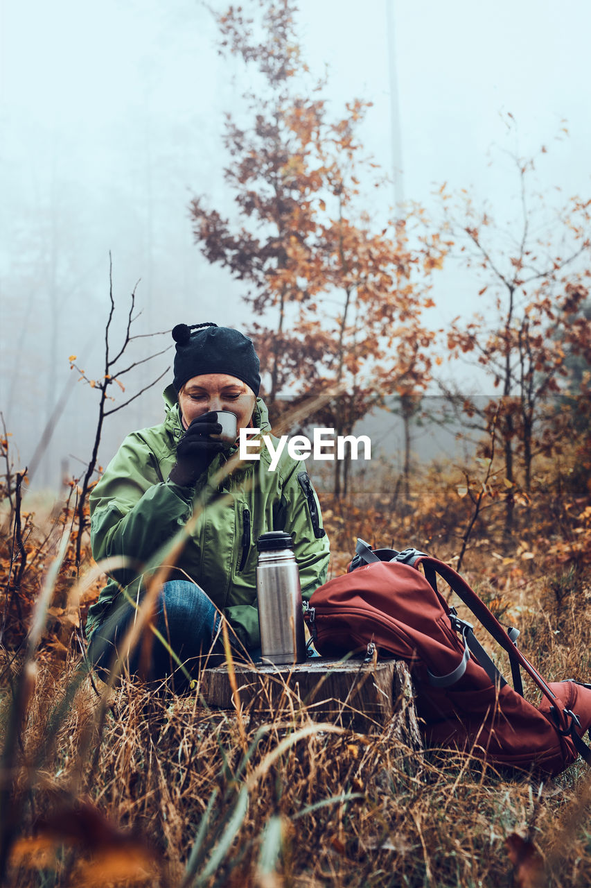 Woman with backpack having break during autumn trip drinking a hot drink from thermos flask