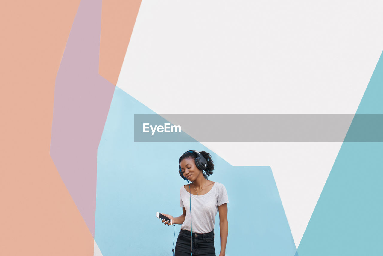 Young woman listening music against colored background