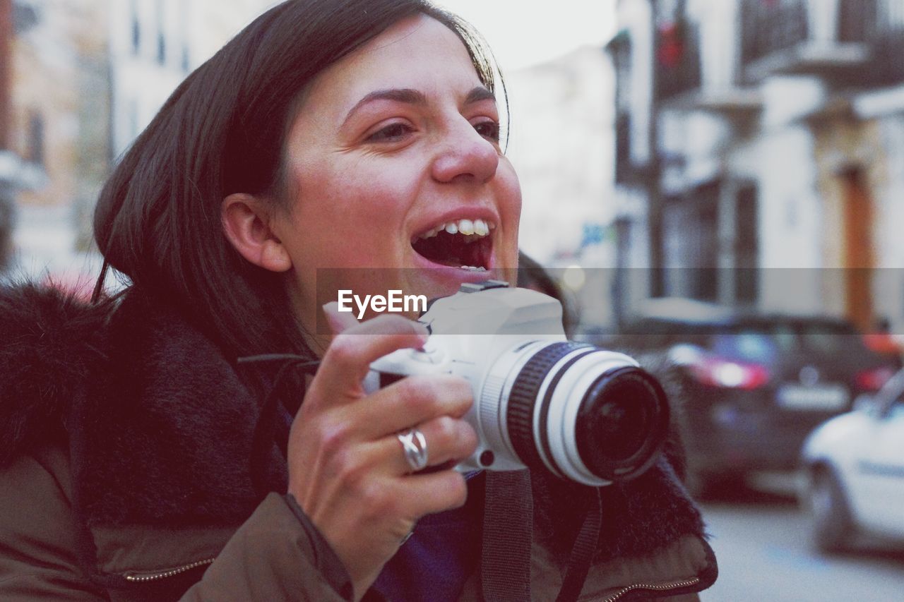 Close-up of cheerful young woman holding camera in city