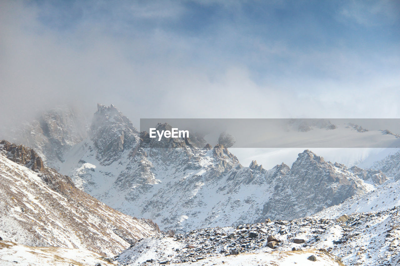 Peaked rocky snow-capped ridge peaks in cloudy fog in tuyuk-su gorge in sunny winter weather