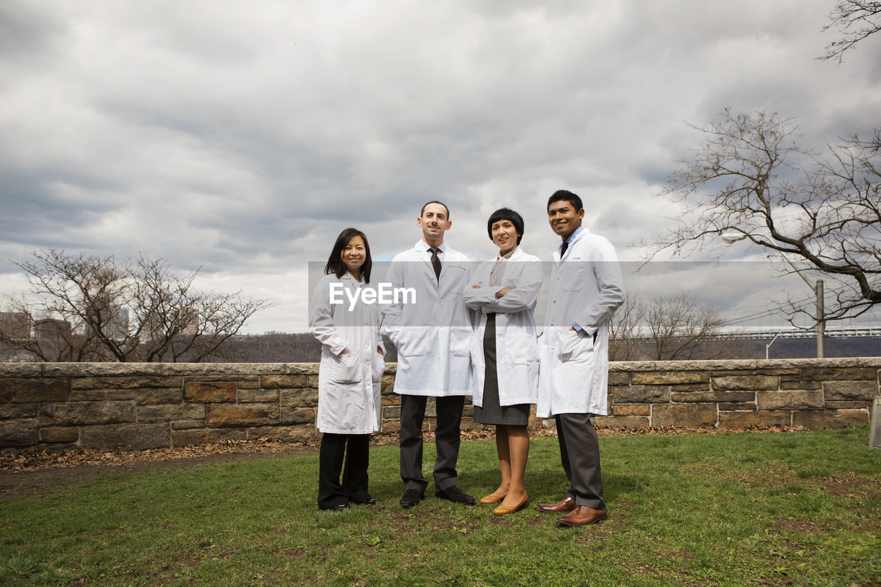 Portrait of doctors standing on field against cloudy sky