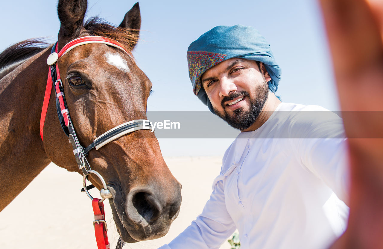 Portrait of smiling man with horse against clear sky