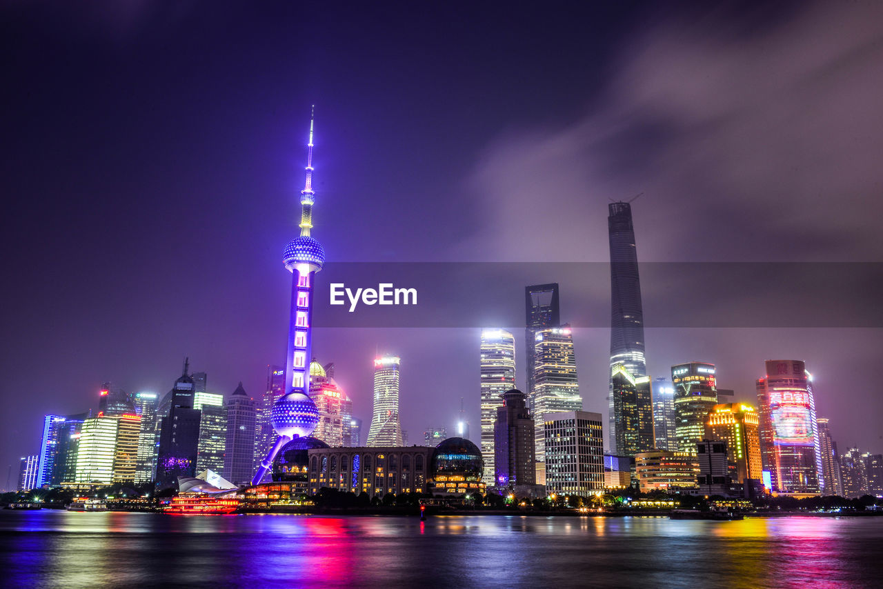 Illuminated oriental pearl tower in city by river huangpu at night