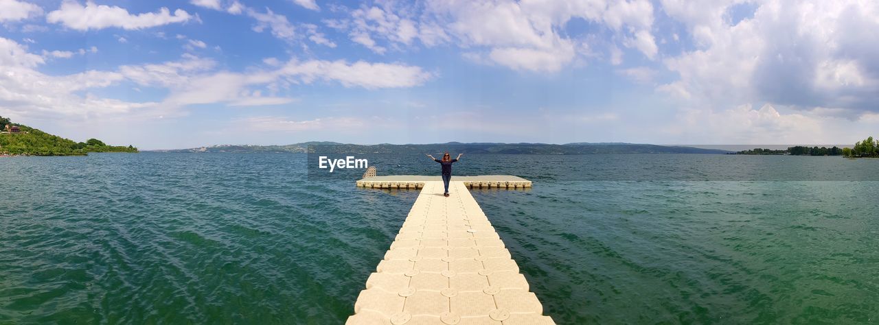 Mid distant view of woman standing on pier against sky