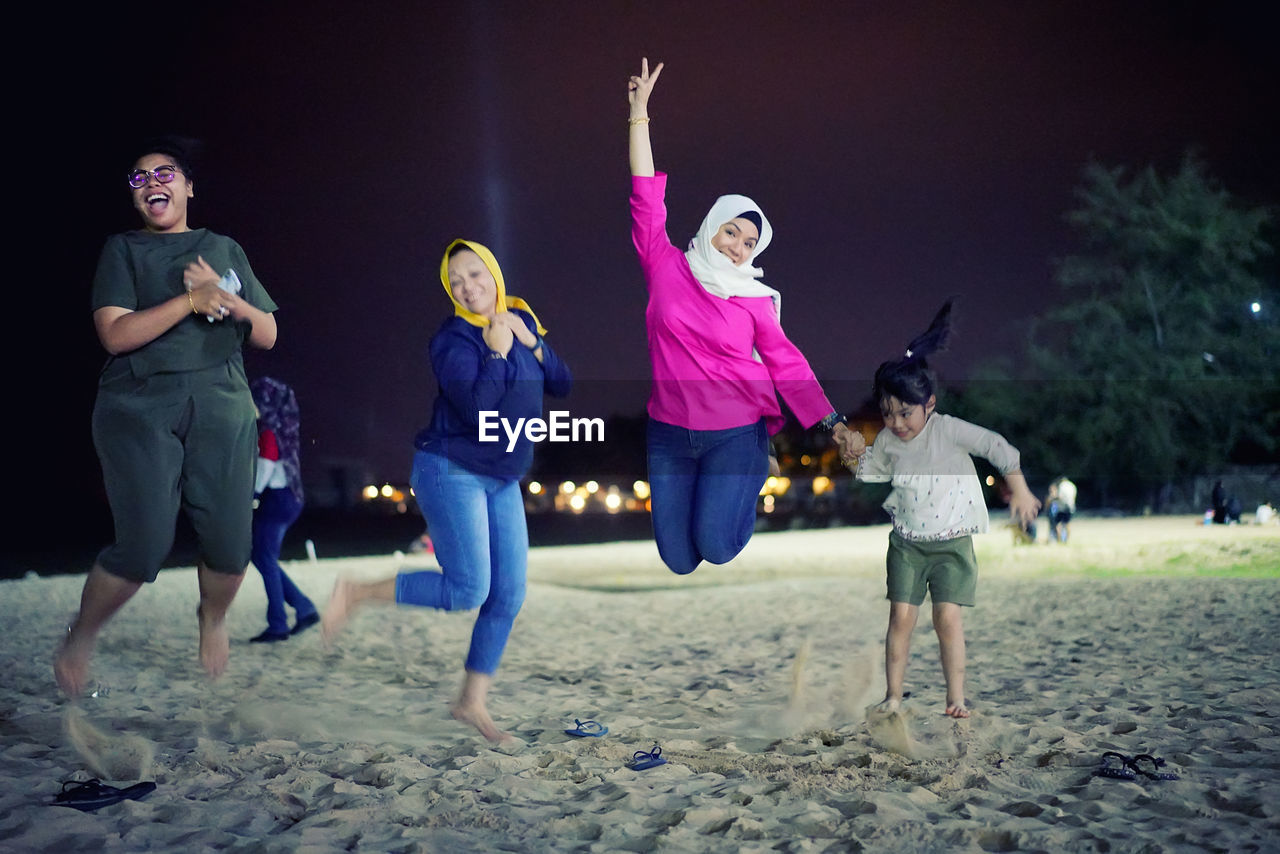 Happy family jumping on beach against sky at night