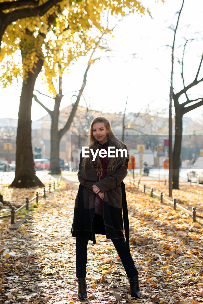 Portrait of young woman standing against trees during autumn