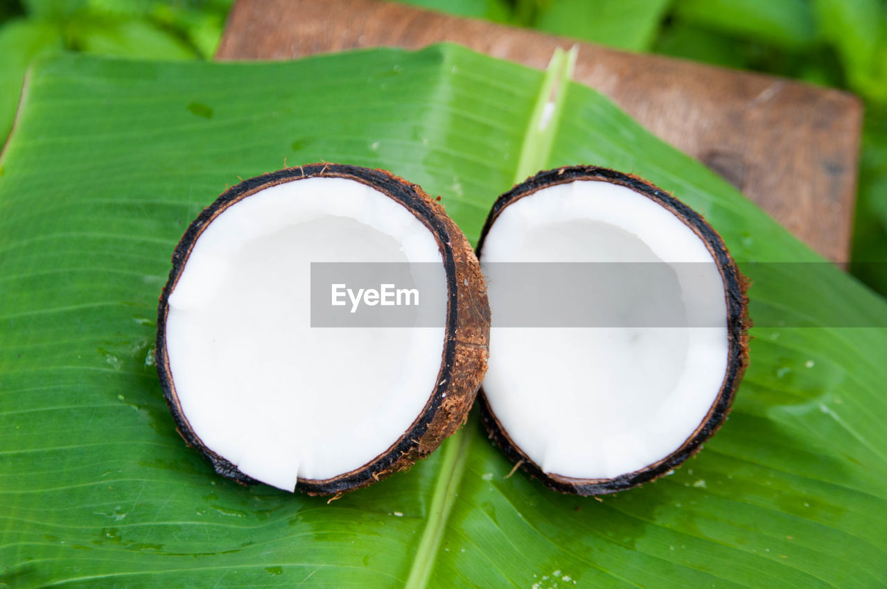 Close-up of halved coconut with banana leaf on stool