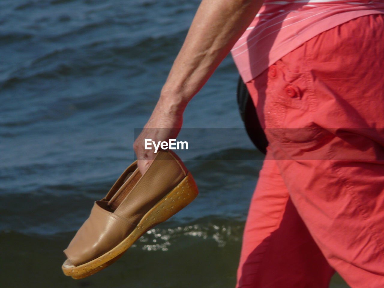 MIDSECTION OF MAN HOLDING WHILE STANDING BY SEA AGAINST SKY