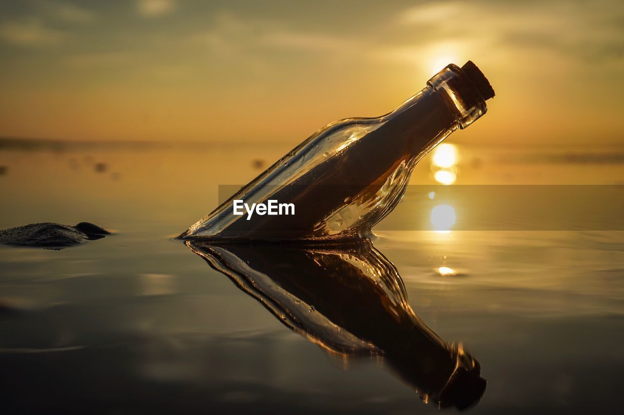 Close-up of bottle floating on water against sunset sky