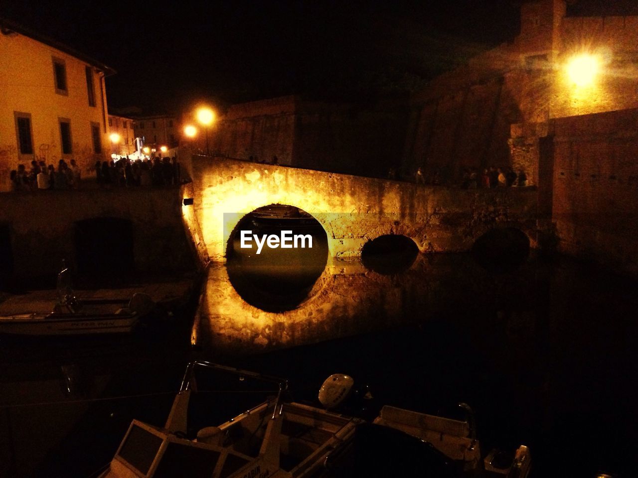 Illuminated bridge over canal amidst buildings at night