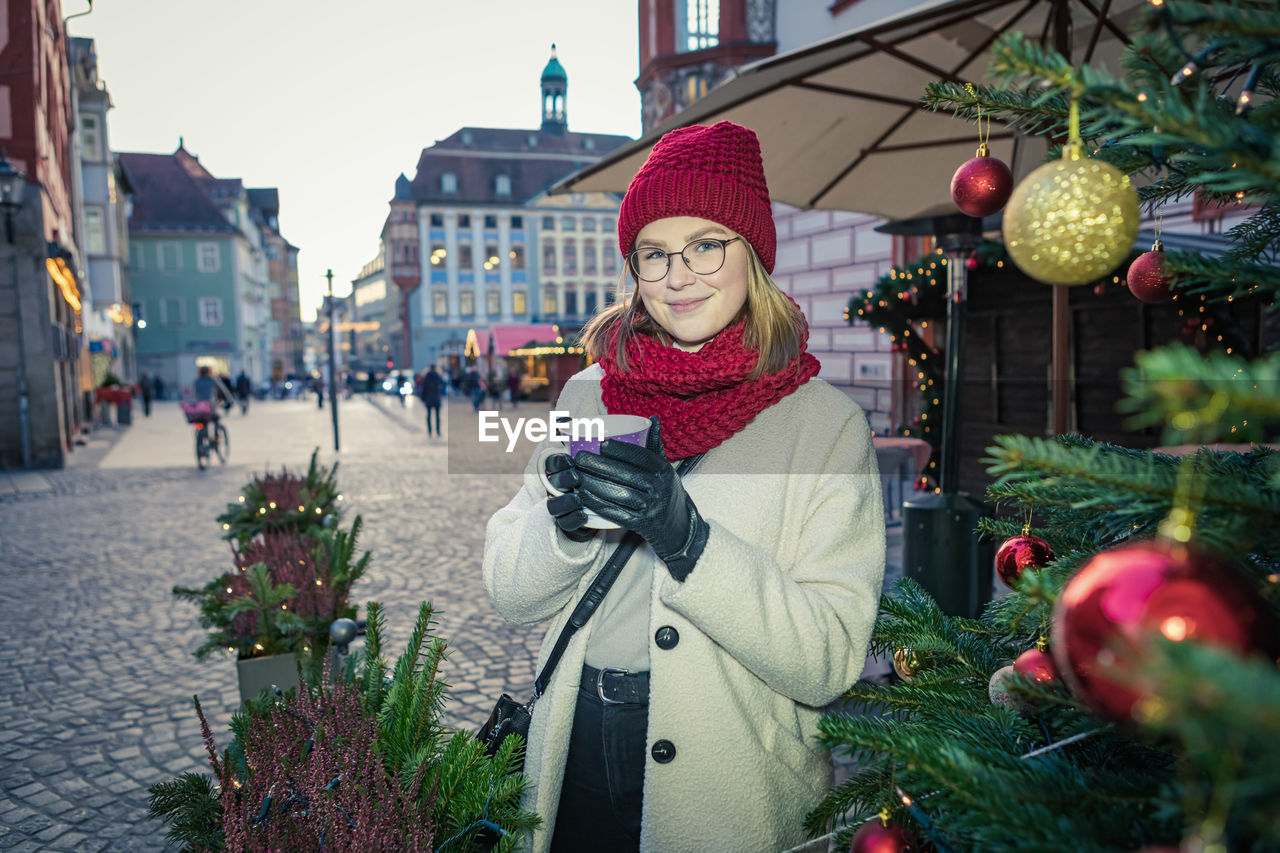 Portrait of smiling woman holding drink on street in city during christmas