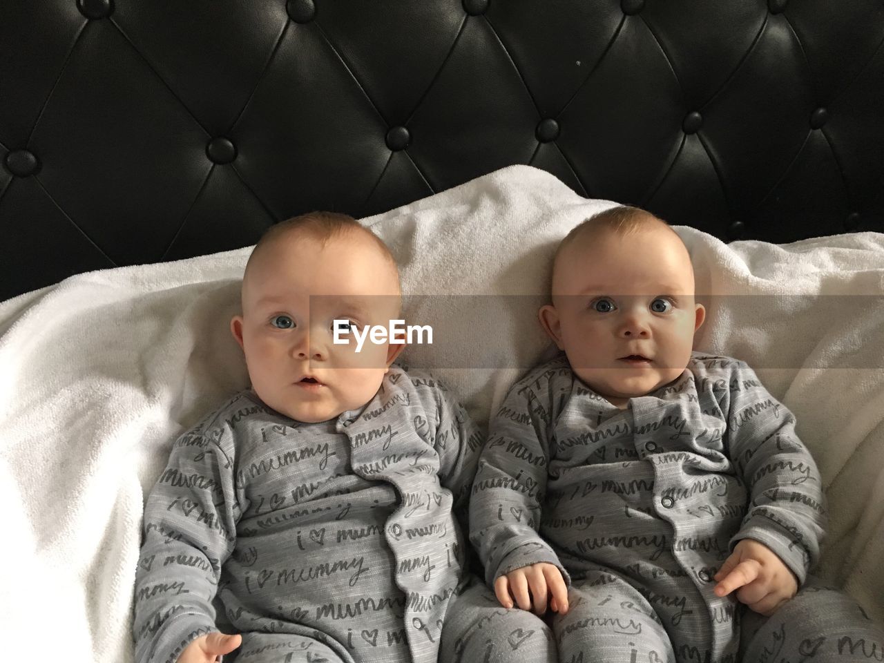 Portrait of cute twins sitting on bed at home