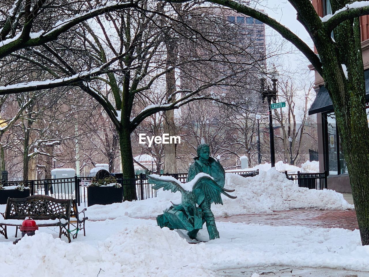 BARE TREES ON SNOW COVERED PARK BENCH