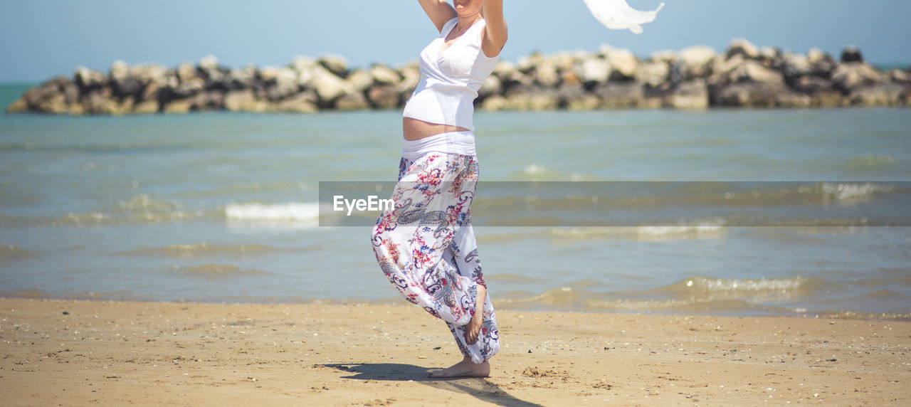 Low section of playful pregnant woman standing at beach