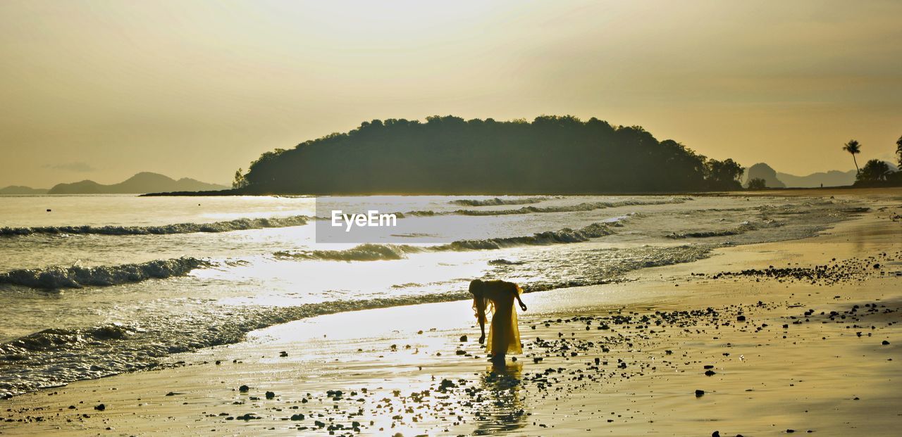 MAN STANDING ON BEACH AGAINST SKY DURING SUNSET