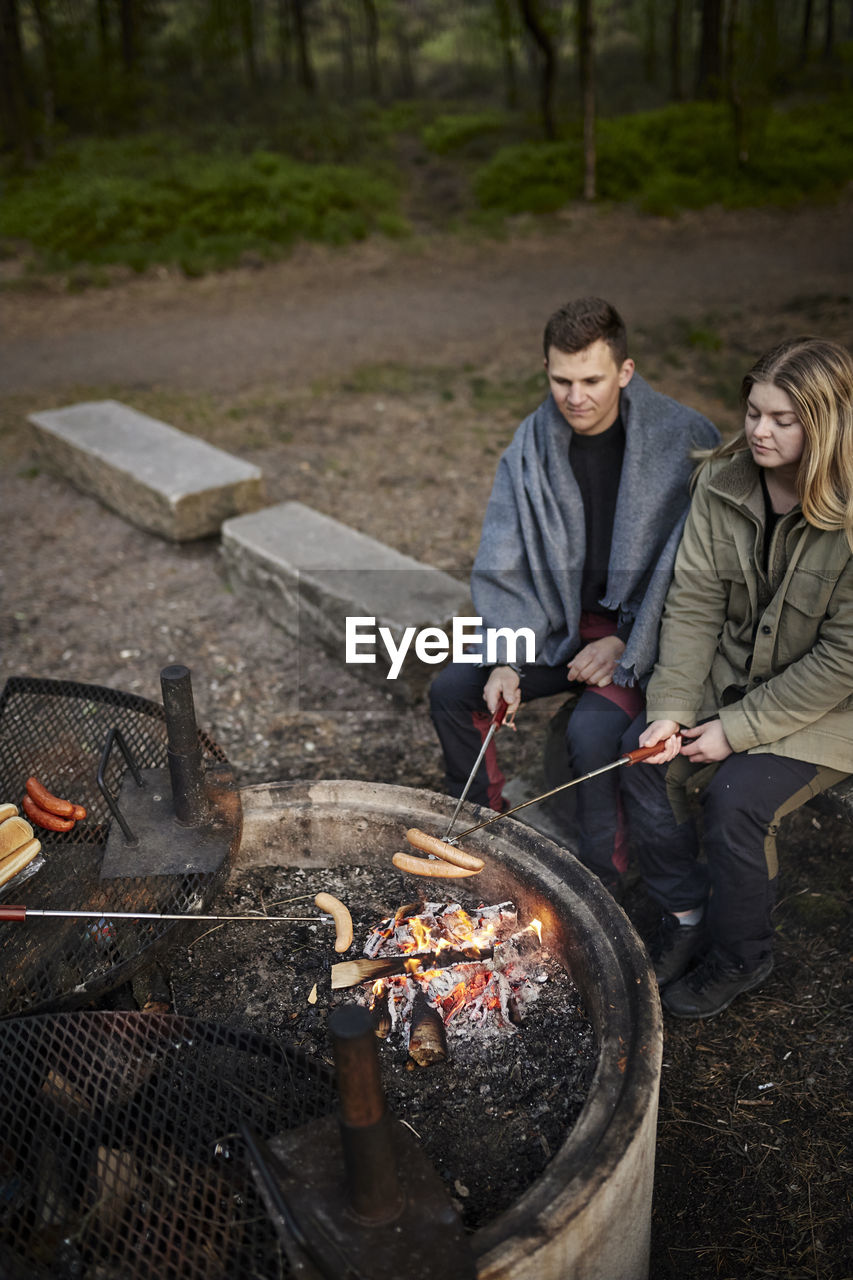 Couple preparing hotdogs over campfire