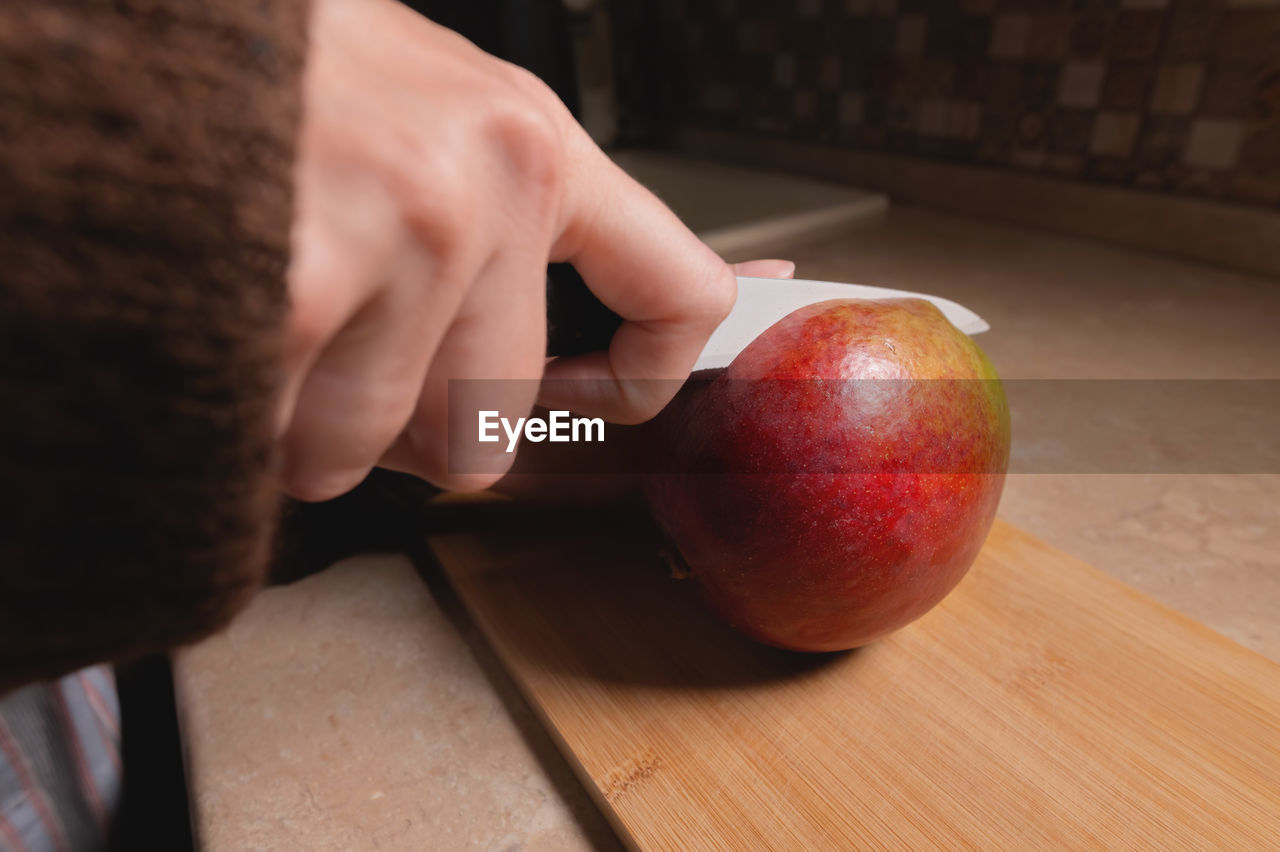 Close-up of woman's hands cutting fresh mango on wooden cutting board at home kitchen