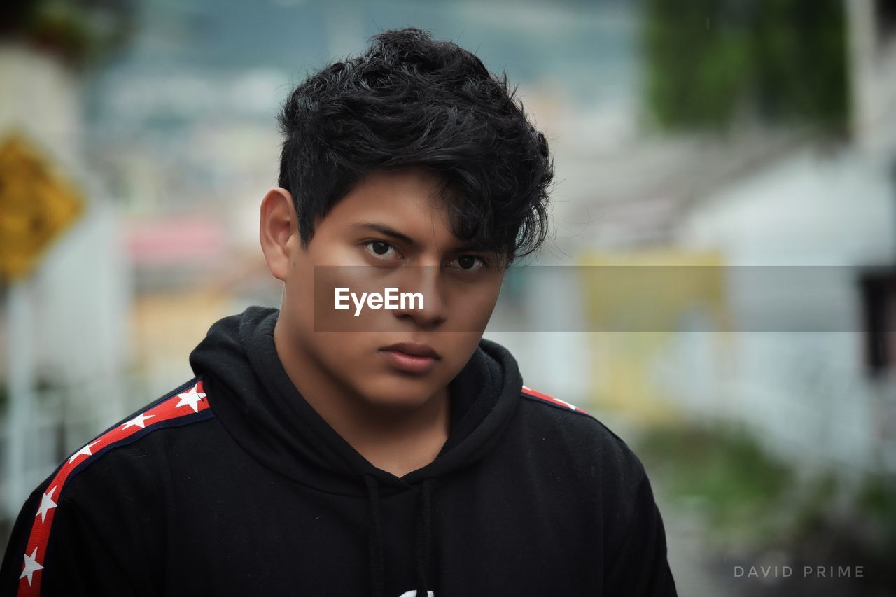 Portrait of serious young man wearing black hooded shirt in city