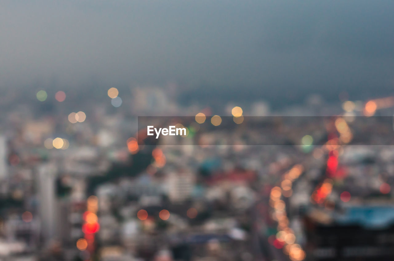 DEFOCUSED IMAGE OF ILLUMINATED CITY AGAINST SKY