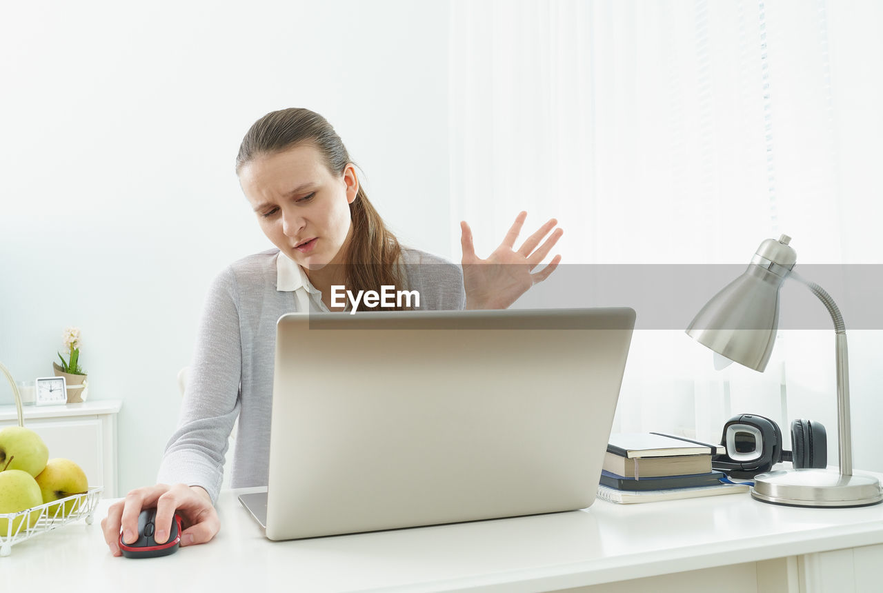 YOUNG WOMAN USING PHONE WHILE SITTING ON LAPTOP