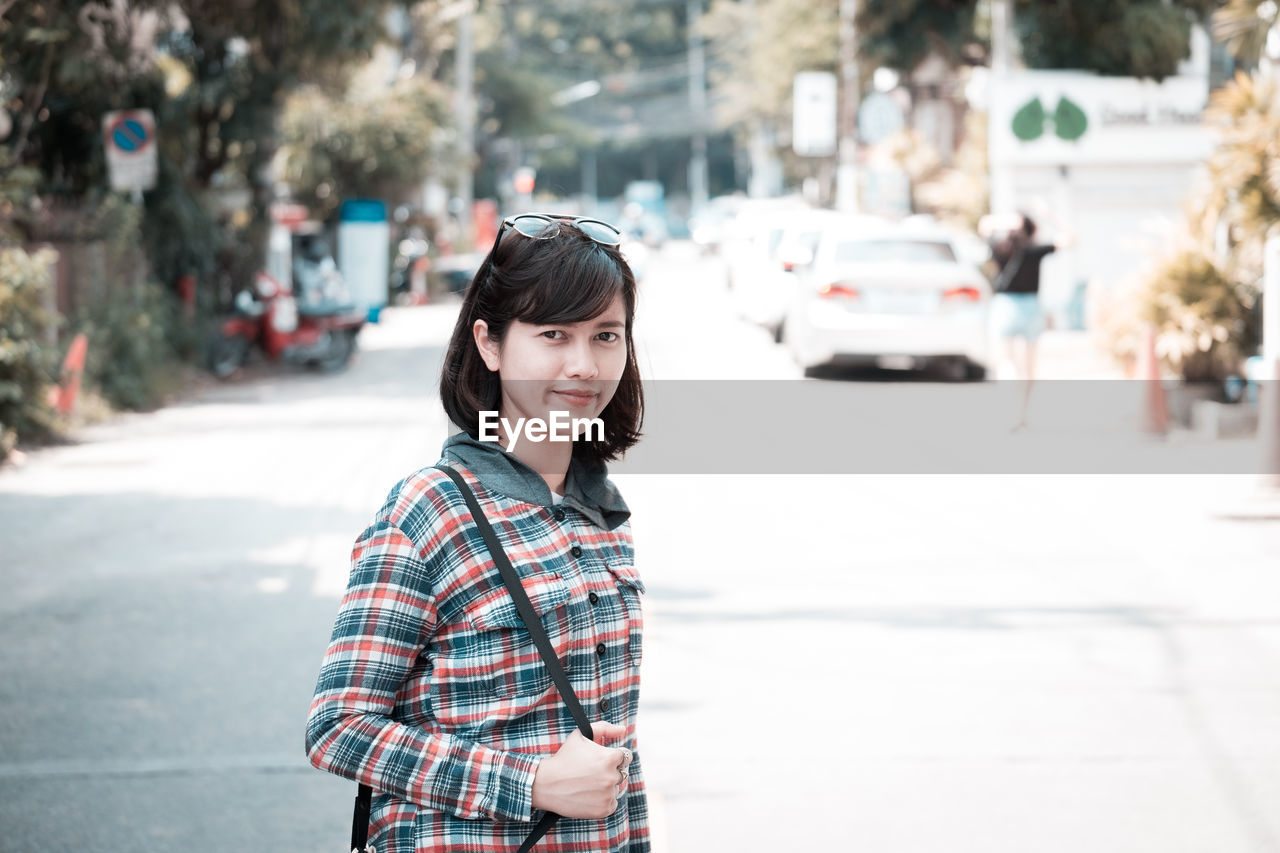 Portrait of smiling young woman standing on road in city