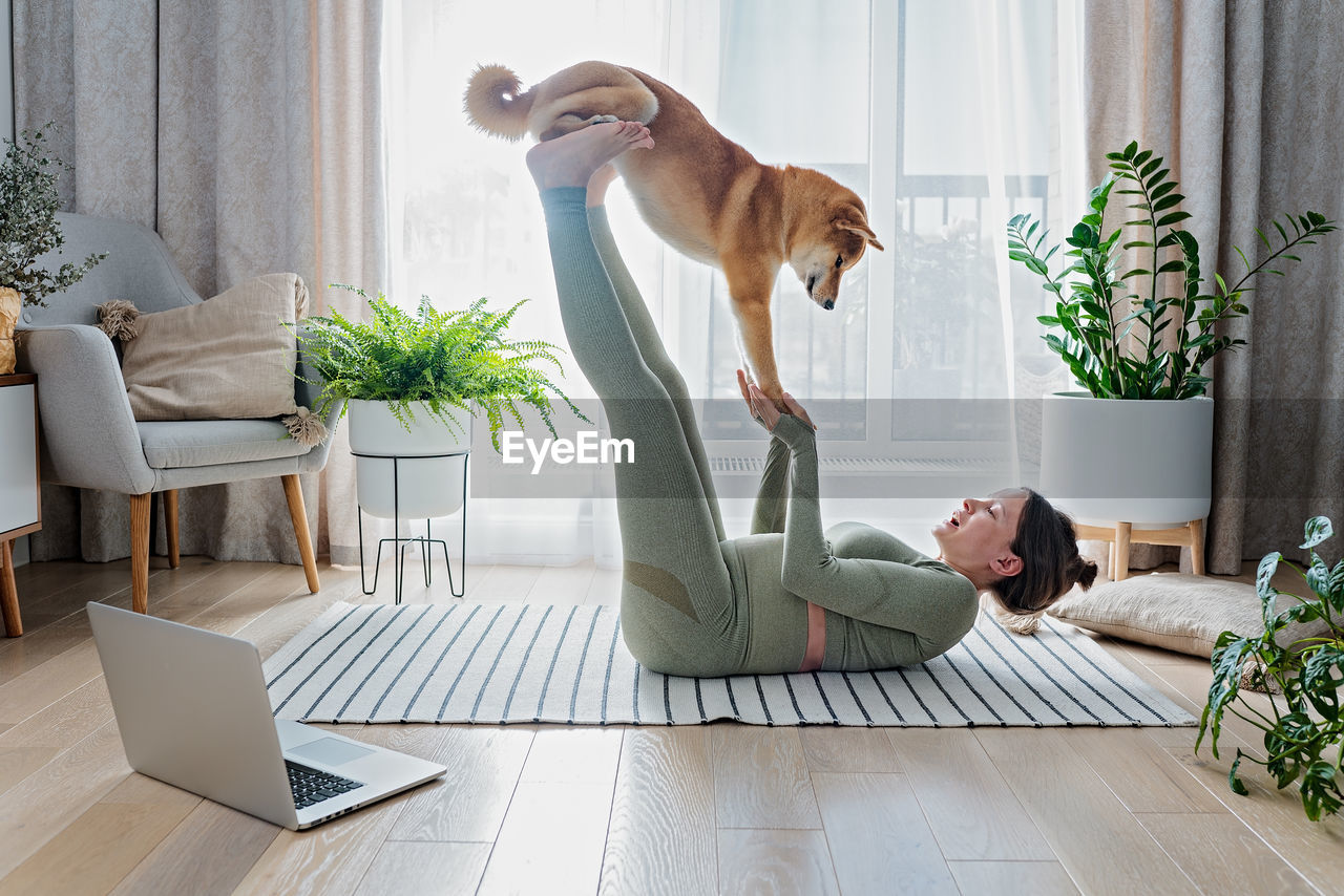 Funny pregnant female doing online yoga with cute shiba inu dog at home. doga yoga or dog training