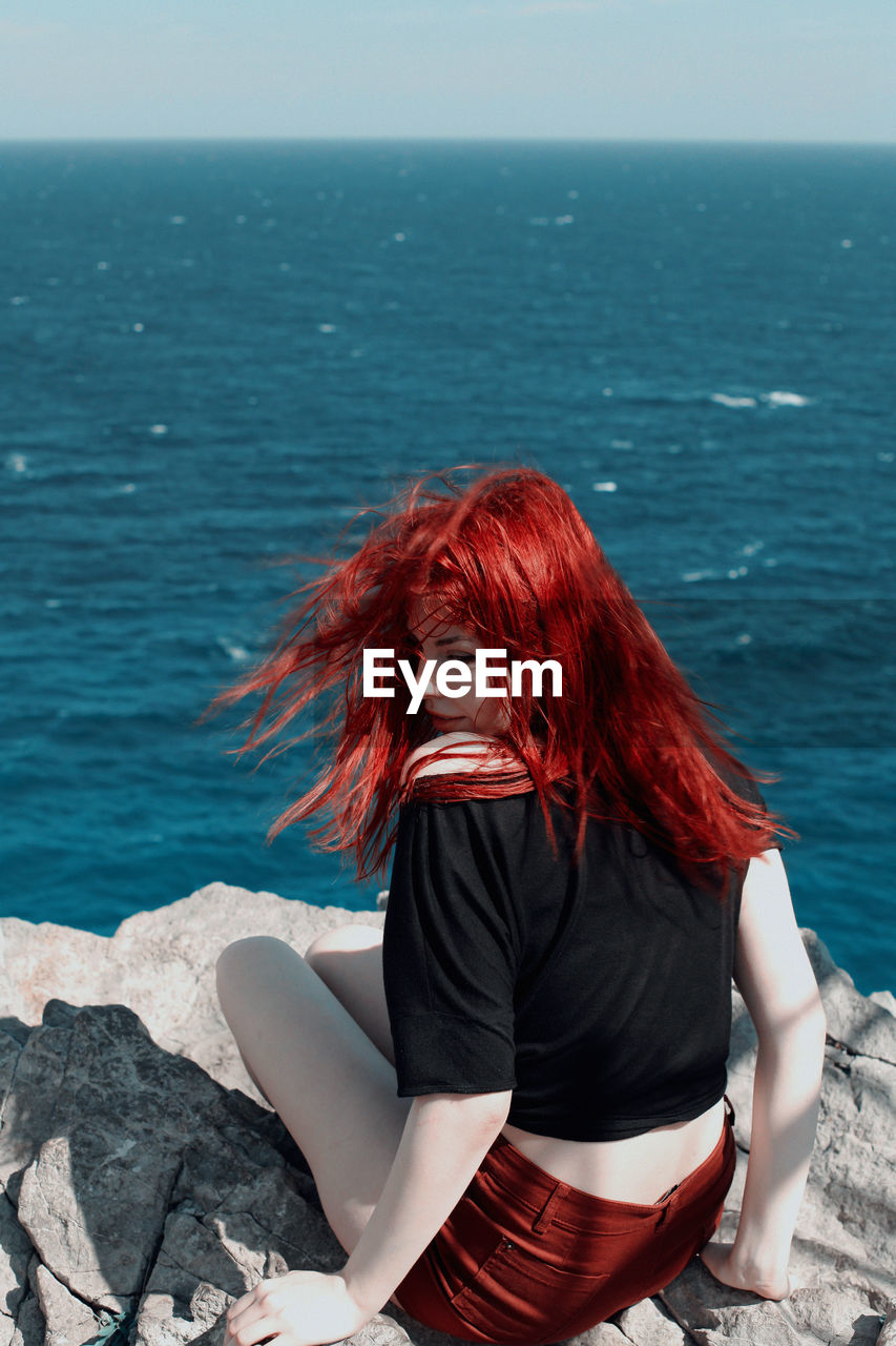Woman with redhead sitting n rock against sea