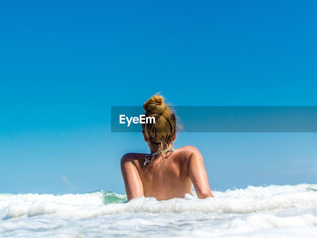 Rear view of young woman lying in sea against sky